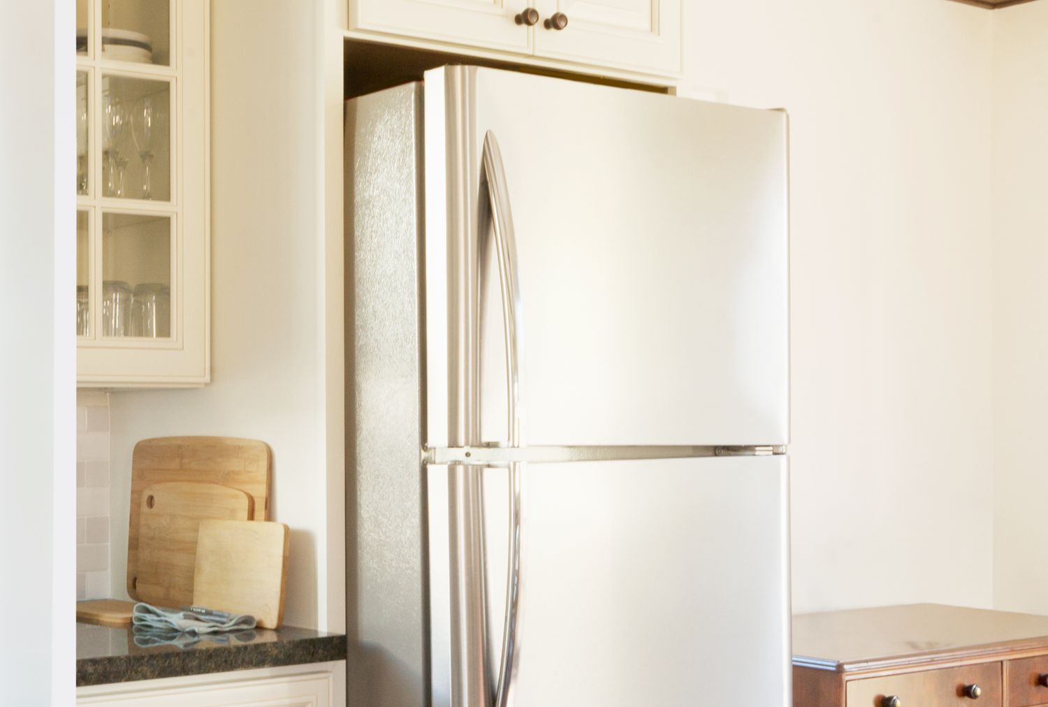 A modern refrigerator positioned in a kitchen next to cabinetry and a countertop with cutting boards