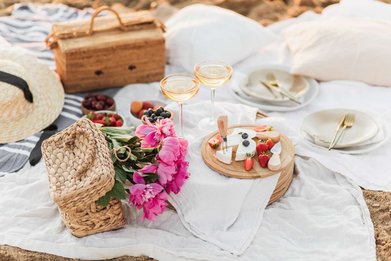 Picnic setup with flowers basket food and glasses on a blanket outdoors