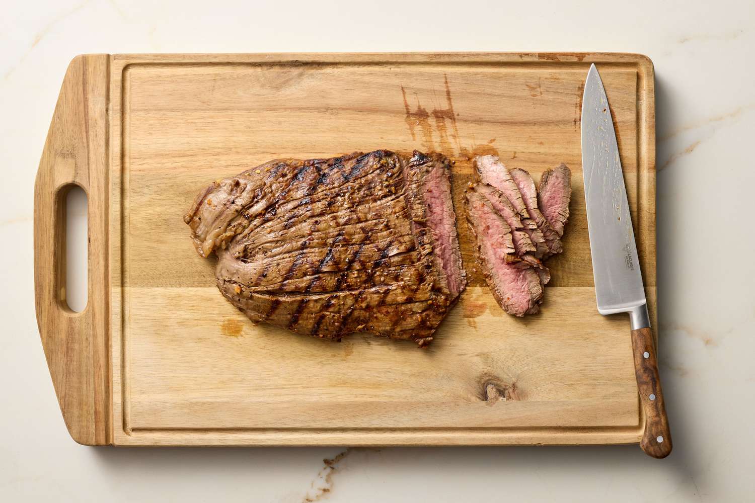 Cooked flank steak sliced on a wooden cutting board with a knife
