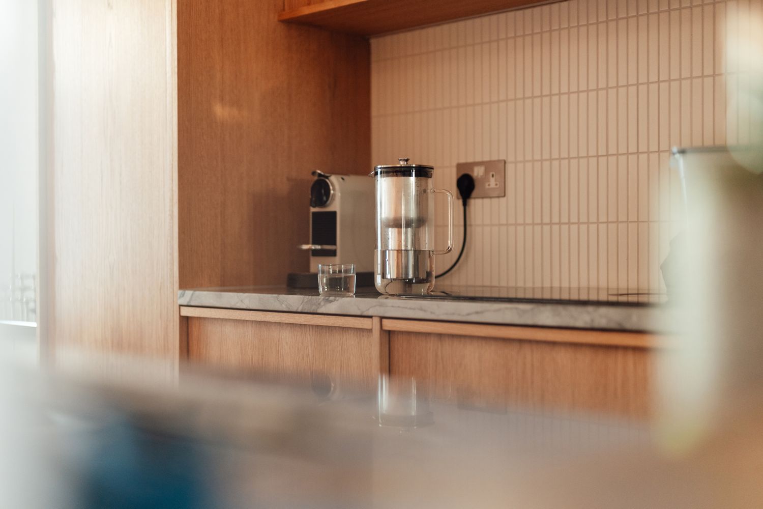 A kitchen counter with a coffee maker and a glass water pitcher on a tiled backsplash wall