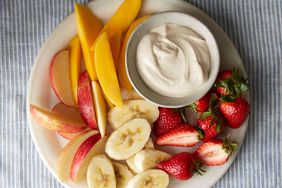 sliced strawberries, bananas, apples, and mango on plate with small bowl of dip