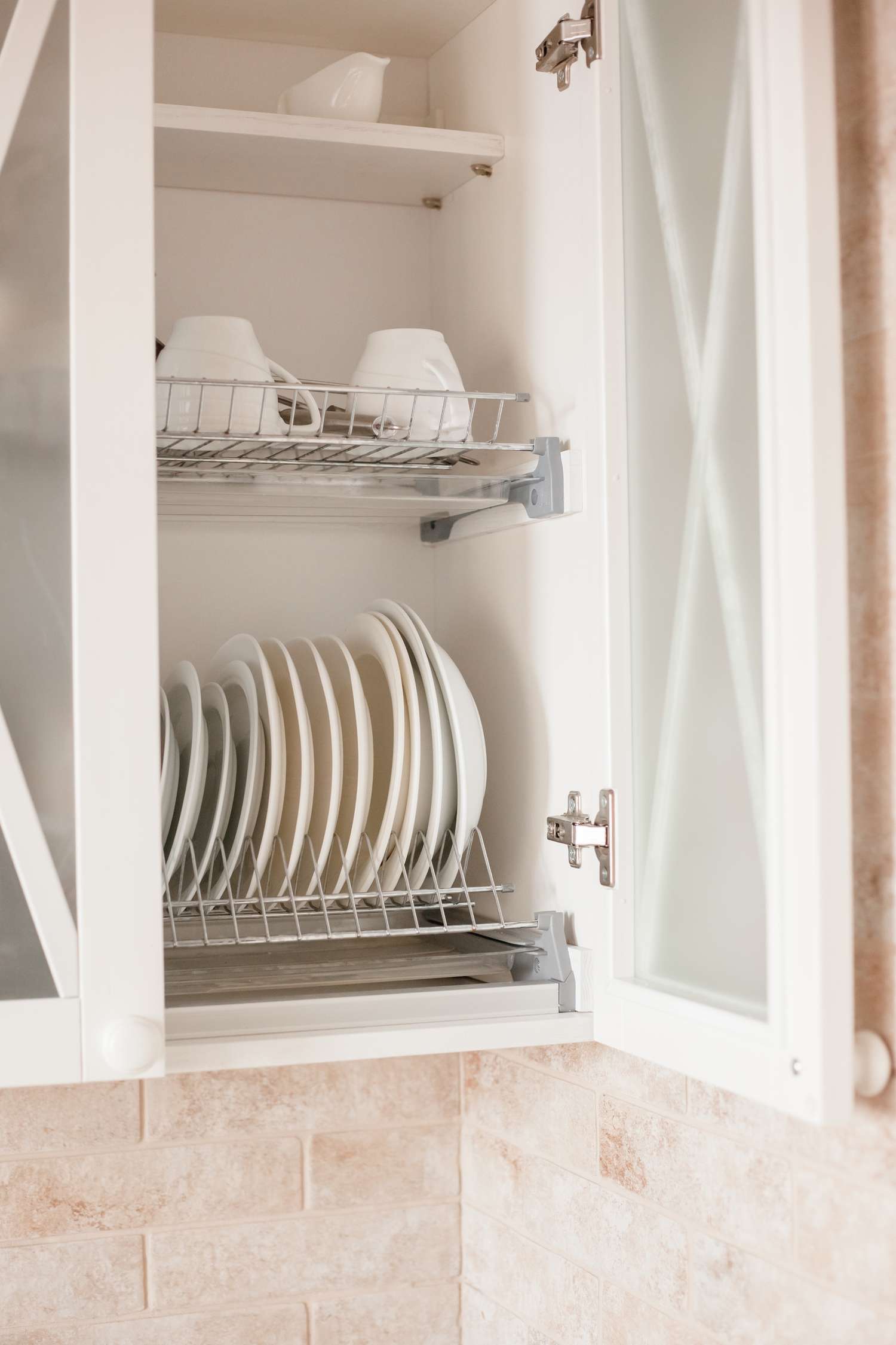 Open kitchen cabinet showing neatly arranged dishes and cups on wire racks