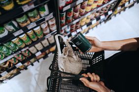 Person holding a canned item in a supermarket placing it into a shopping basket