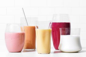 An assortment of smoothies in various glasses displayed on a white tile background
