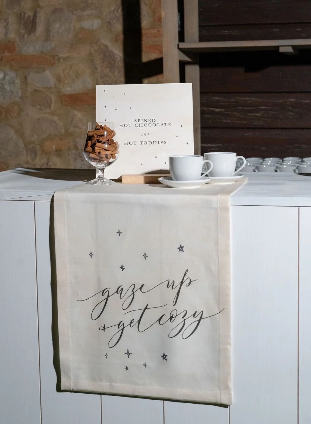 A decorative display setup with a towel featuring calligraphy text and a table with coffee cups snacks and a printed sign