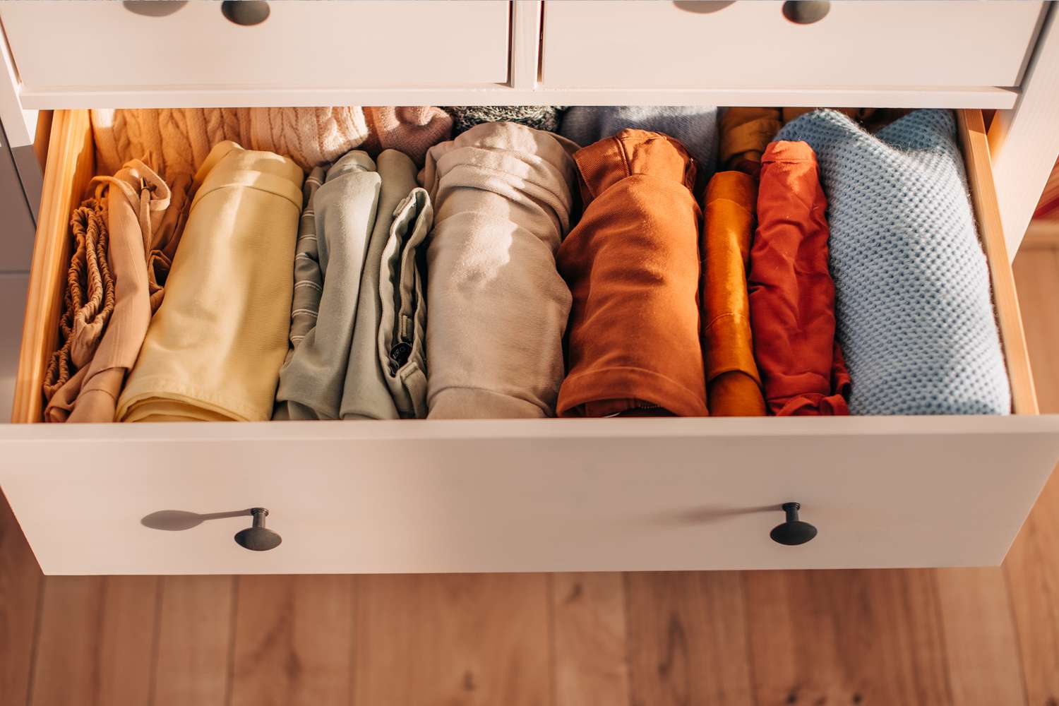 A neatly organized drawer with rolled clothing arranged by type or color