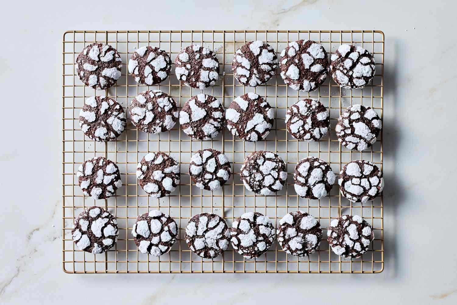 Chocolate crackle cookies on a cooling rack coated with powdered sugar and arranged in neat rows