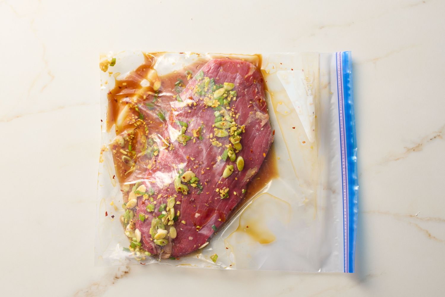 A flank steak marinating in a plastic sealable bag with herbs and seasonings