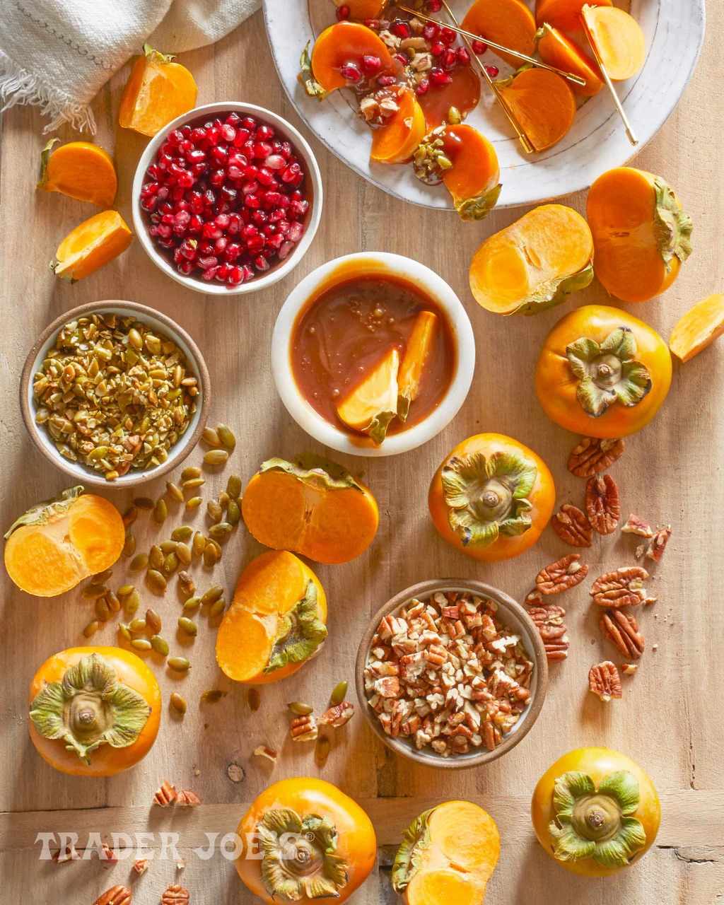 A variety of persimmons nuts and pomegranate seeds displayed on a table with a bowl of fruit dip