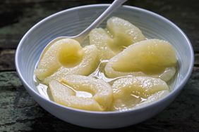 A bowl containing poached pear halves with a spoon