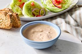 A bowl of Russian dressing with a plate of lettuce wedges and bread slices in the background