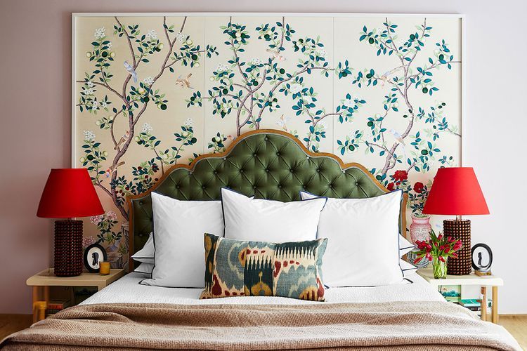 A master bedroom with a tufted headboard decorative pillows red lamps and a naturethemed wall panel