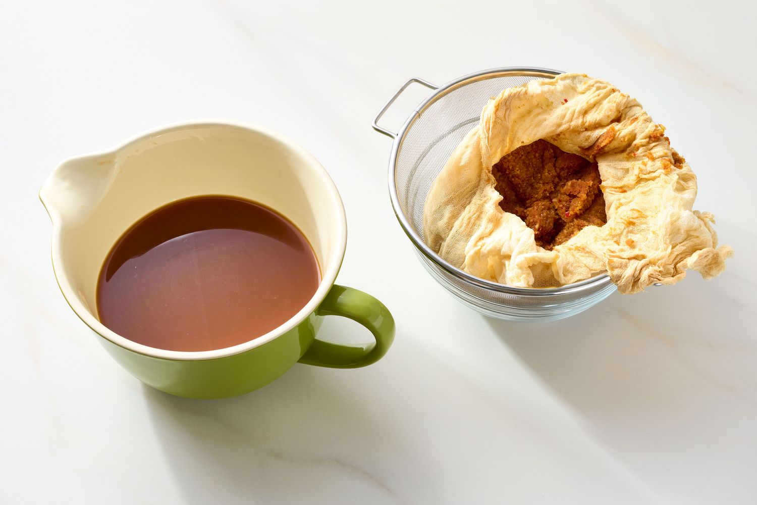 A cup of strained apple cider next to a mesh cloth with pressed apple pulp