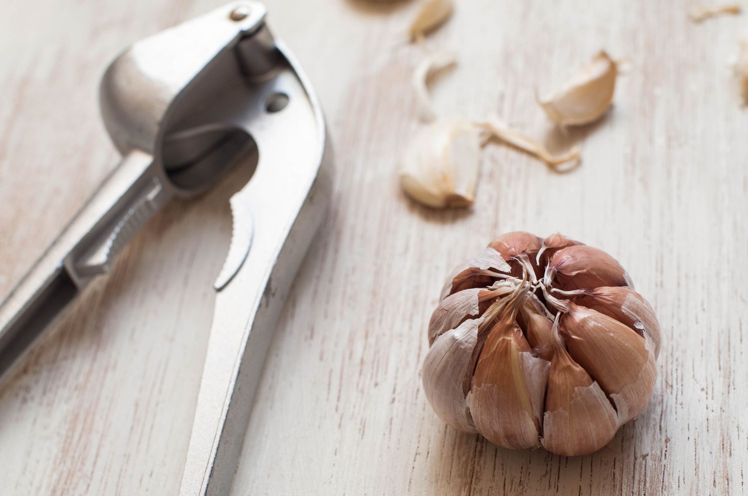Still life of whole garlic clove and garlic press on a white wooden table