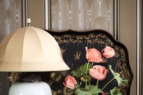 A table lamp a vase with flowers a decorative tray and small objects placed on a wooden surface