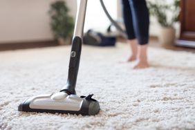 Young woman using a vacuum cleaner while cleaning carpet in the house.