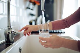 A person filling a glass with water from a kitchen faucet