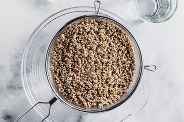 A sieve containing rinsed grains over a clear bowl