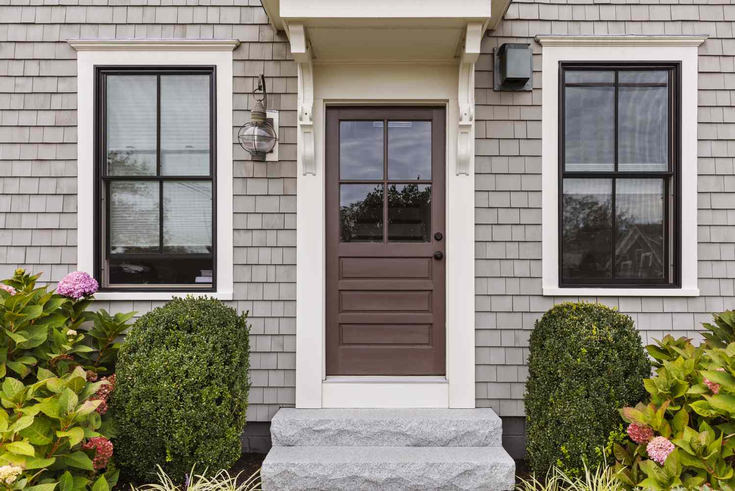 A front door flanked by two windows framed by plants and shingle siding