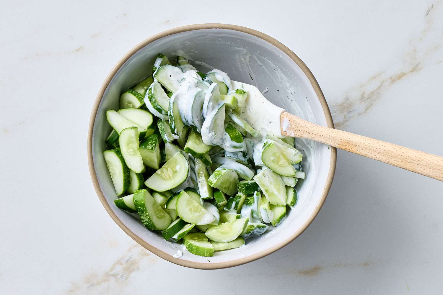 Bowl of cucumber salad mixed with sour cream and dill, a wooden spoon included in the bowl