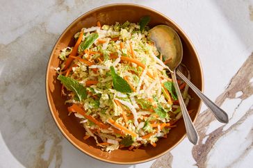 Bowl of napa cabbage slaw garnished with mint leaves and a serving spoon and fork placed inside the bowl