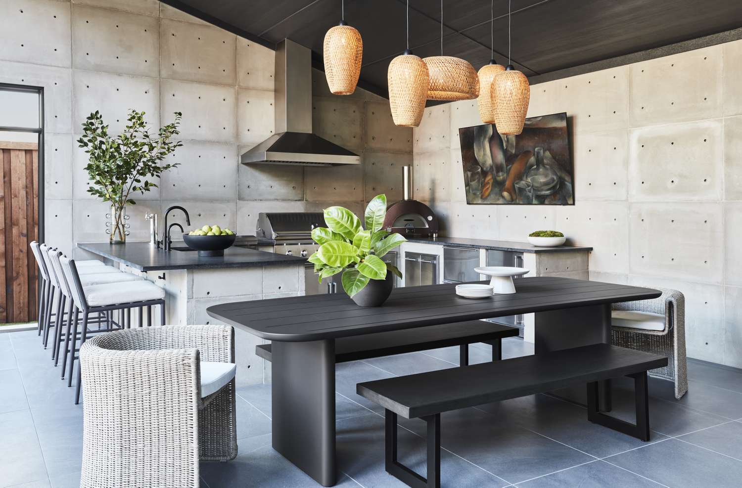 Modern outdoor kitchen and dining area with dark furniture and wicker chairs pendant lighting and plants as decor