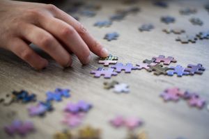 A hand placing a piece in a partially completed jigsaw puzzle