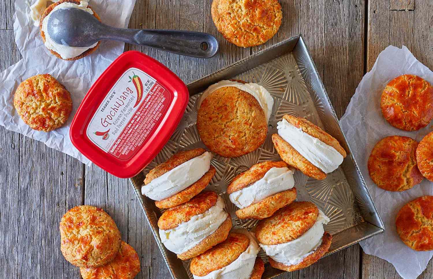 Ice cream sandwiches made with biscuits and a tub of ice cream on a wooden surface