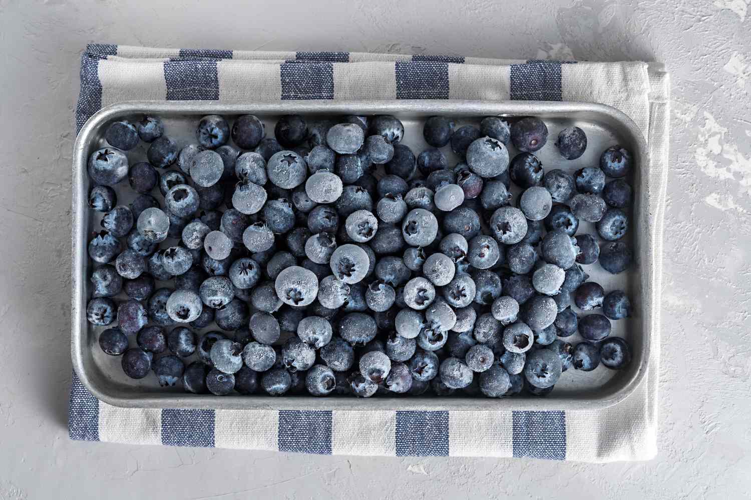 frozen blueberries on a baking sheet with a striped kitchen cloth underneath