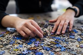 Hands sorting through jigsaw puzzle pieces on a surface