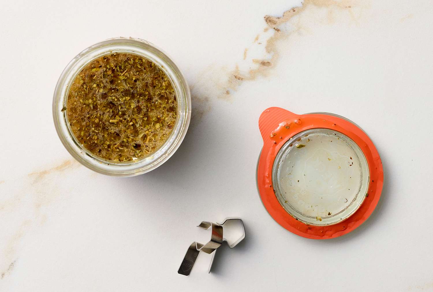 A jar with a mixture, next to a lid and clip, on a marble surface