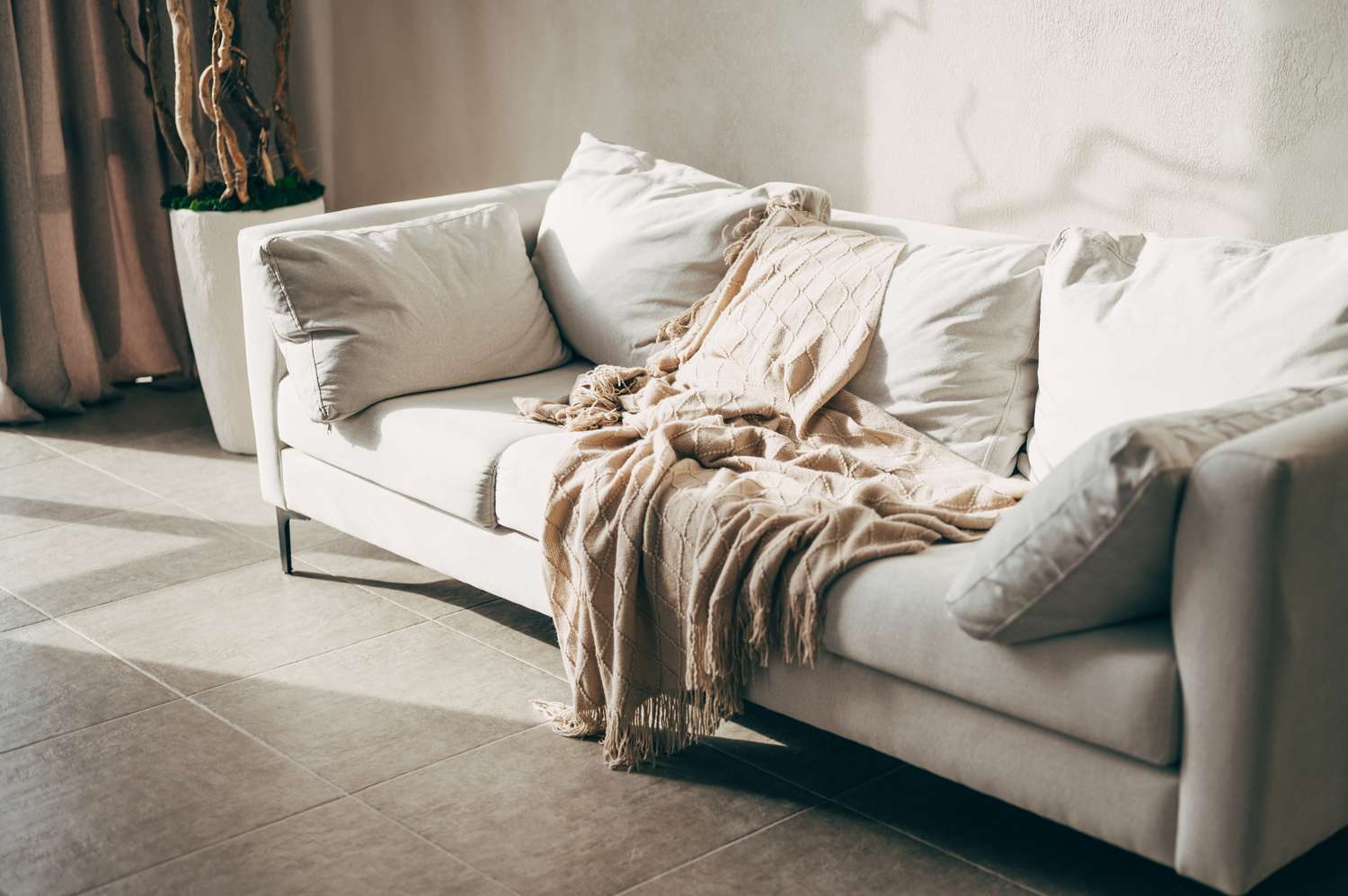 A sofa with cushions and a blanket draped over it in a sunlit room