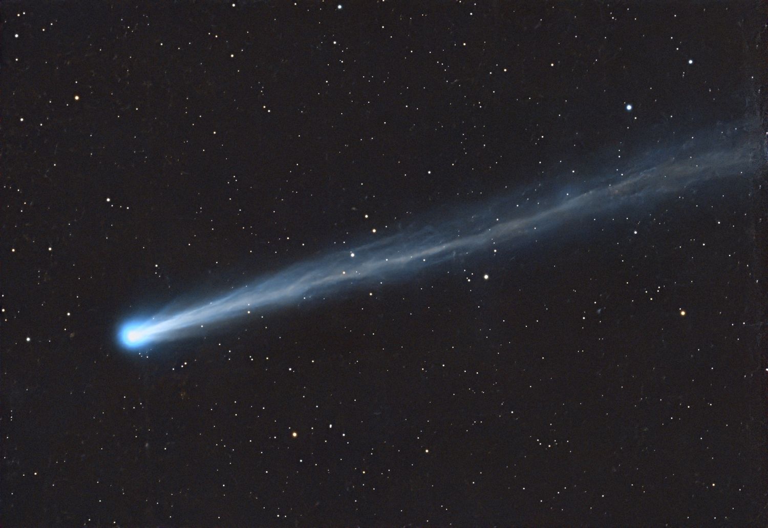A comet streaking across a starfilled night sky showing a bright nucleus and a long tail extending to the right
