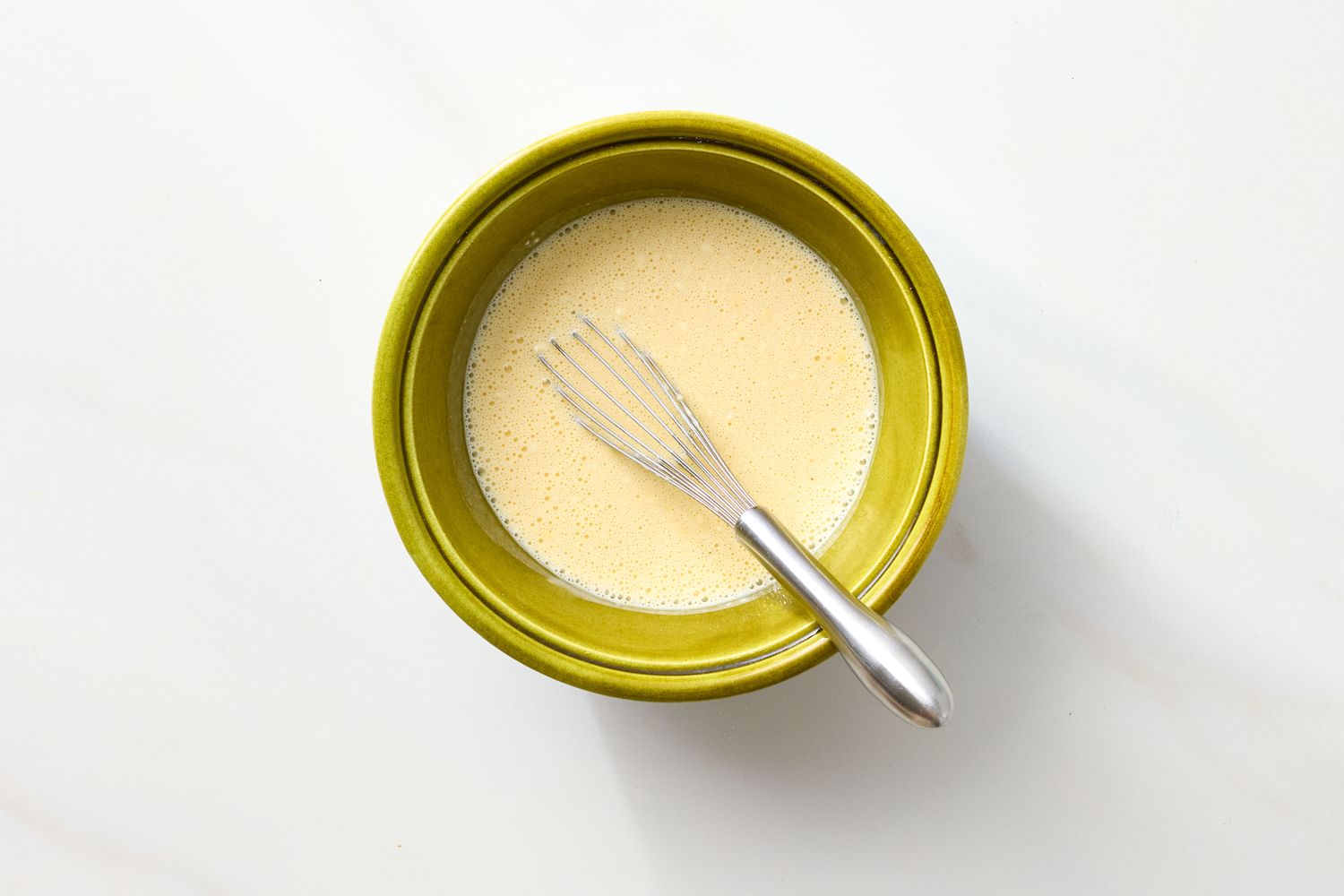 A mixing bowl containing batter with a whisk resting inside