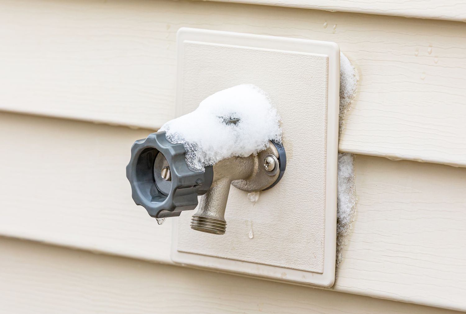 A wallmounted outdoor water spigot with some snow on it