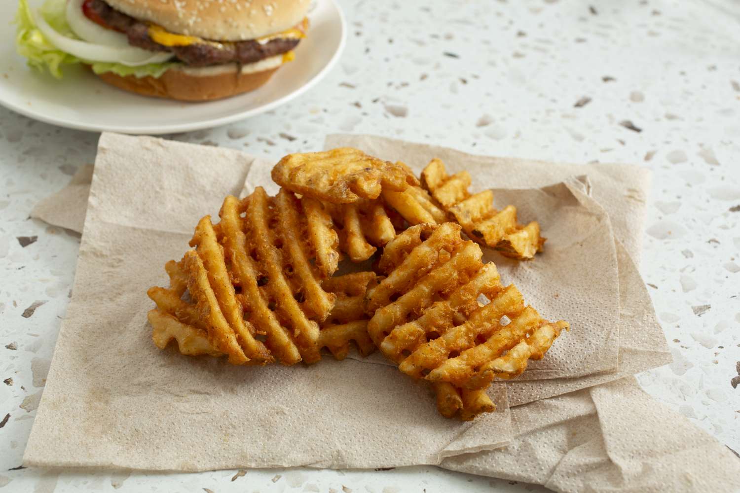 waffle fries on napkin with burger in background