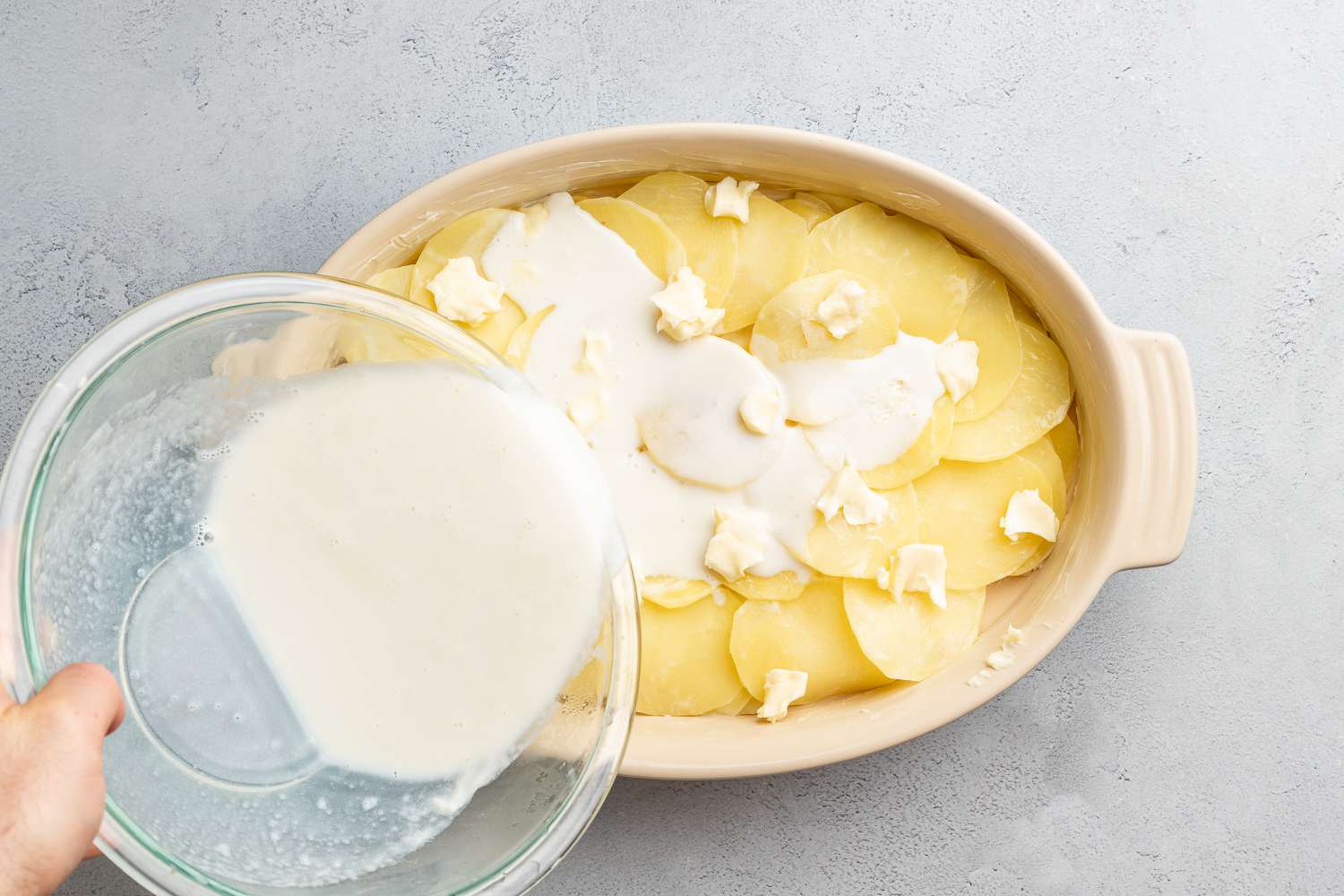 adding milk to sliced potatoes in baking dish