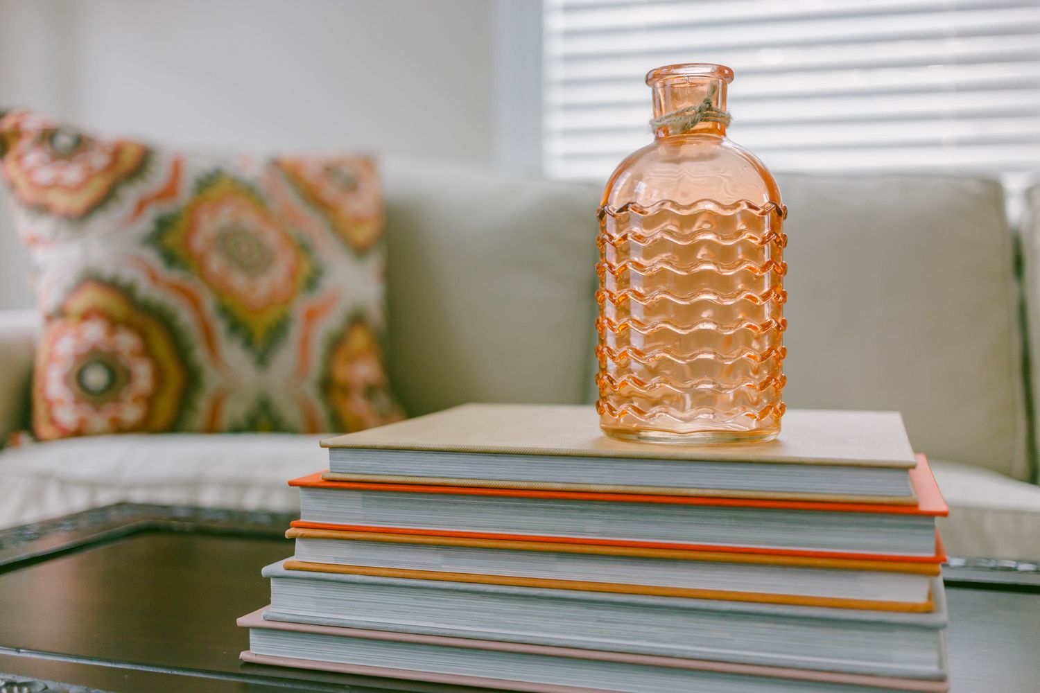 A decorative bottle on a stack of books focus on table items with a sofa in the background