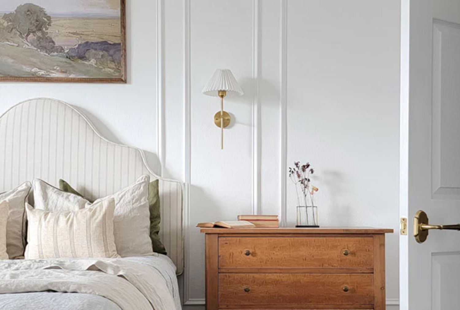 A bedroom with a bed a wooden dresser and a wallmounted lamp featuring minimalist decor