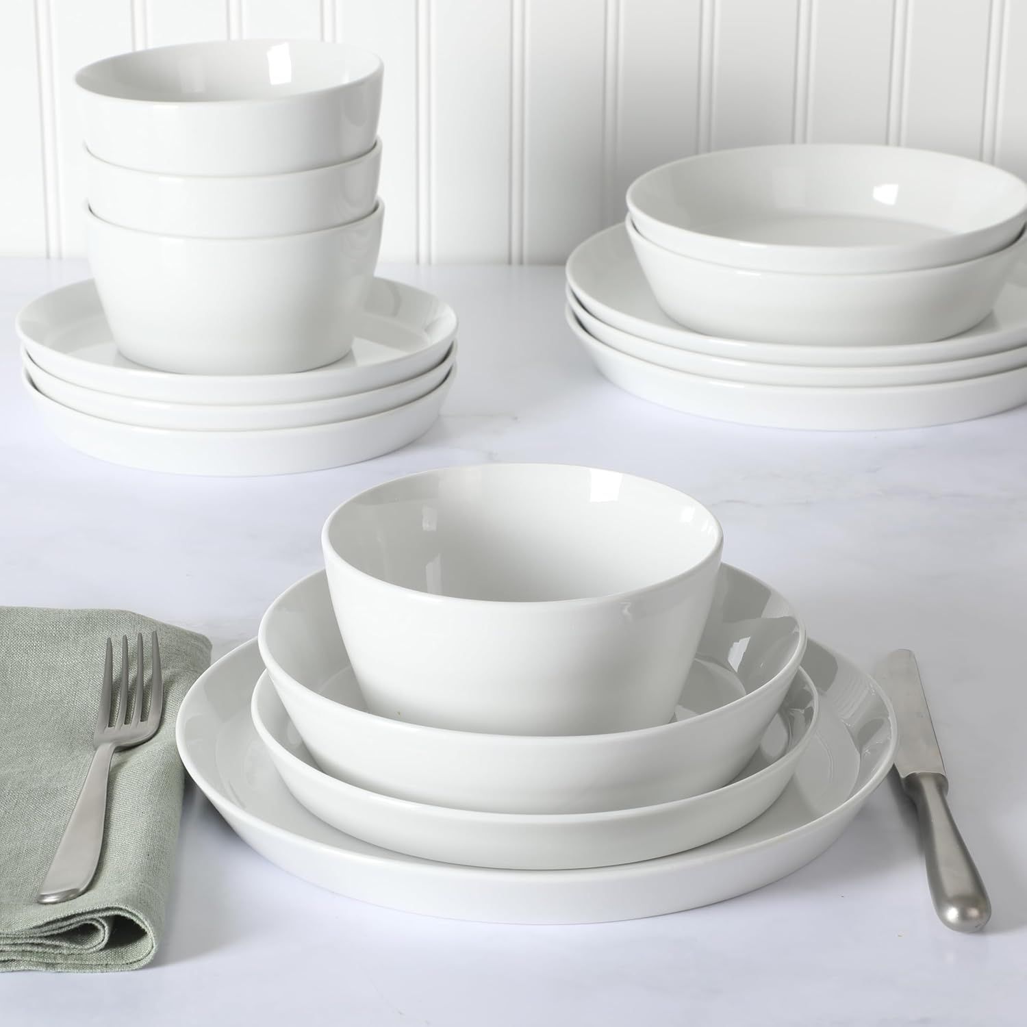Stacked white dinnerware set displayed with a fork knife and napkin