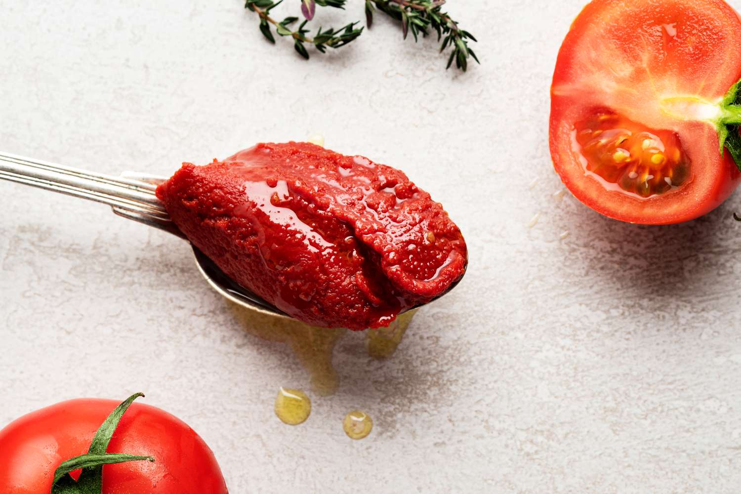 A spoonful of tomato paste with fresh tomatoes and herbs around it