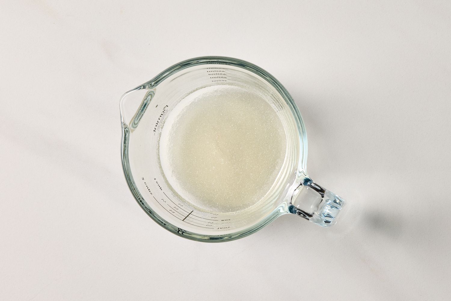 A clear measuring cup with a liquid mixture inside placed on a light surface