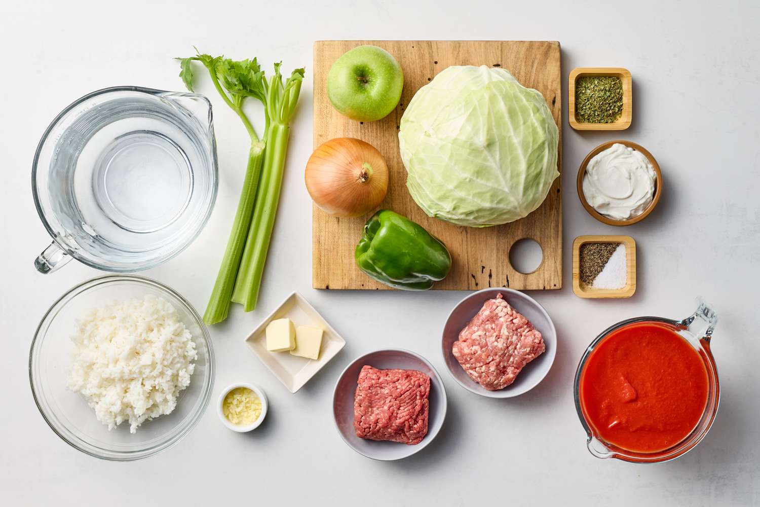 Ingredients for making stuffed cabbage including cabbage ground meat spices tomato sauce rice and vegetables on a cutting board