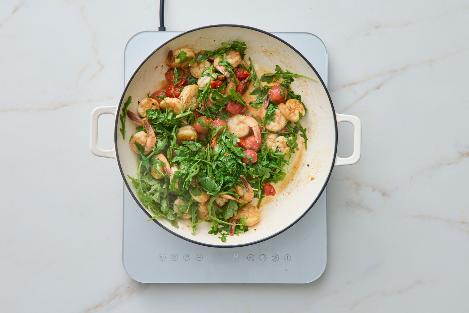 A pan containing sautéed shrimp with arugula and tomatoes on a stove top