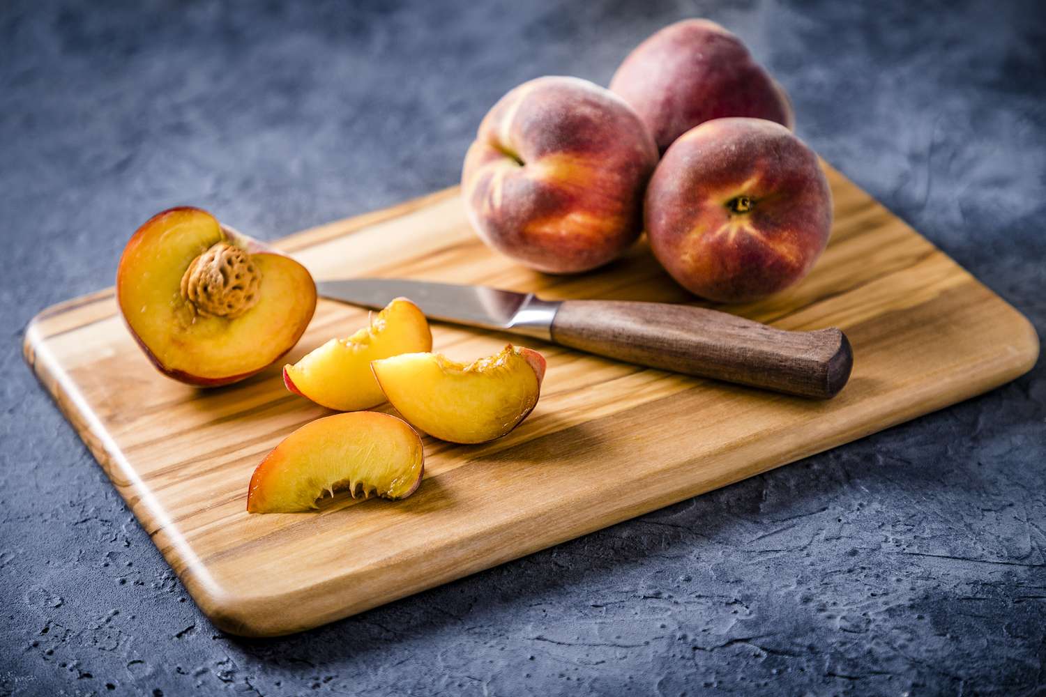 whole and sliced peaches on wooden cutting board with knife