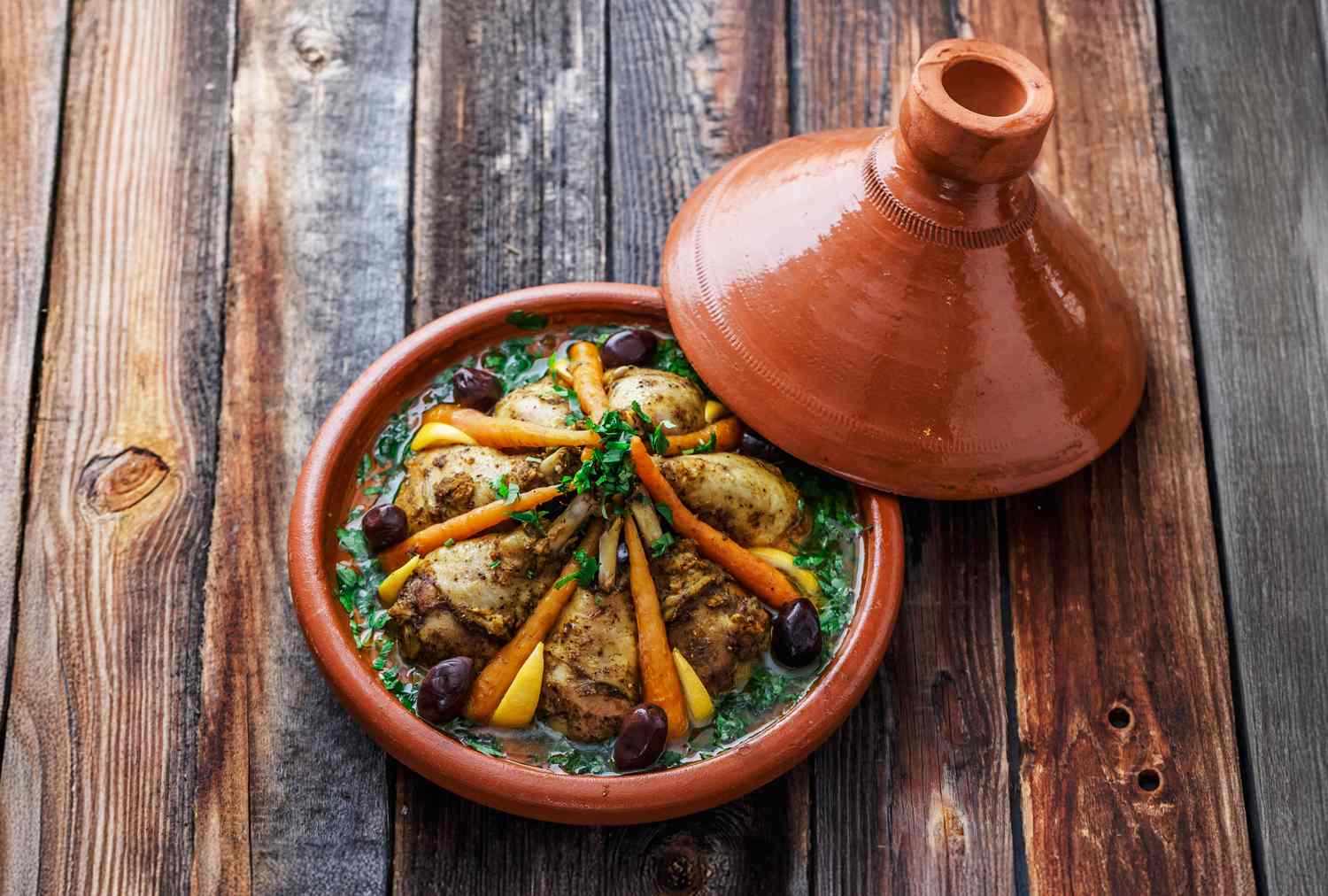 Moroccan tagine with chicken carrots olives and garnishes in a traditional earthenware dish