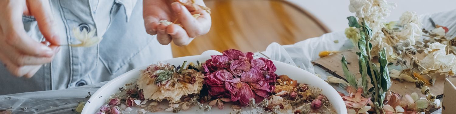 Hands arranging dried flowers on a white surface surrounded by various dried floral pieces