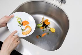 Food scraps being cleared from a plate into a kitchen sink with a garbage disposal