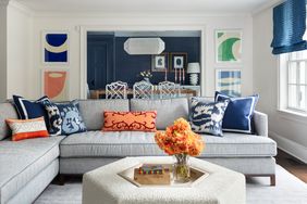 A living room with a sectional sofa decorative pillows a coffee table with flowers and a view of a dining area in the background