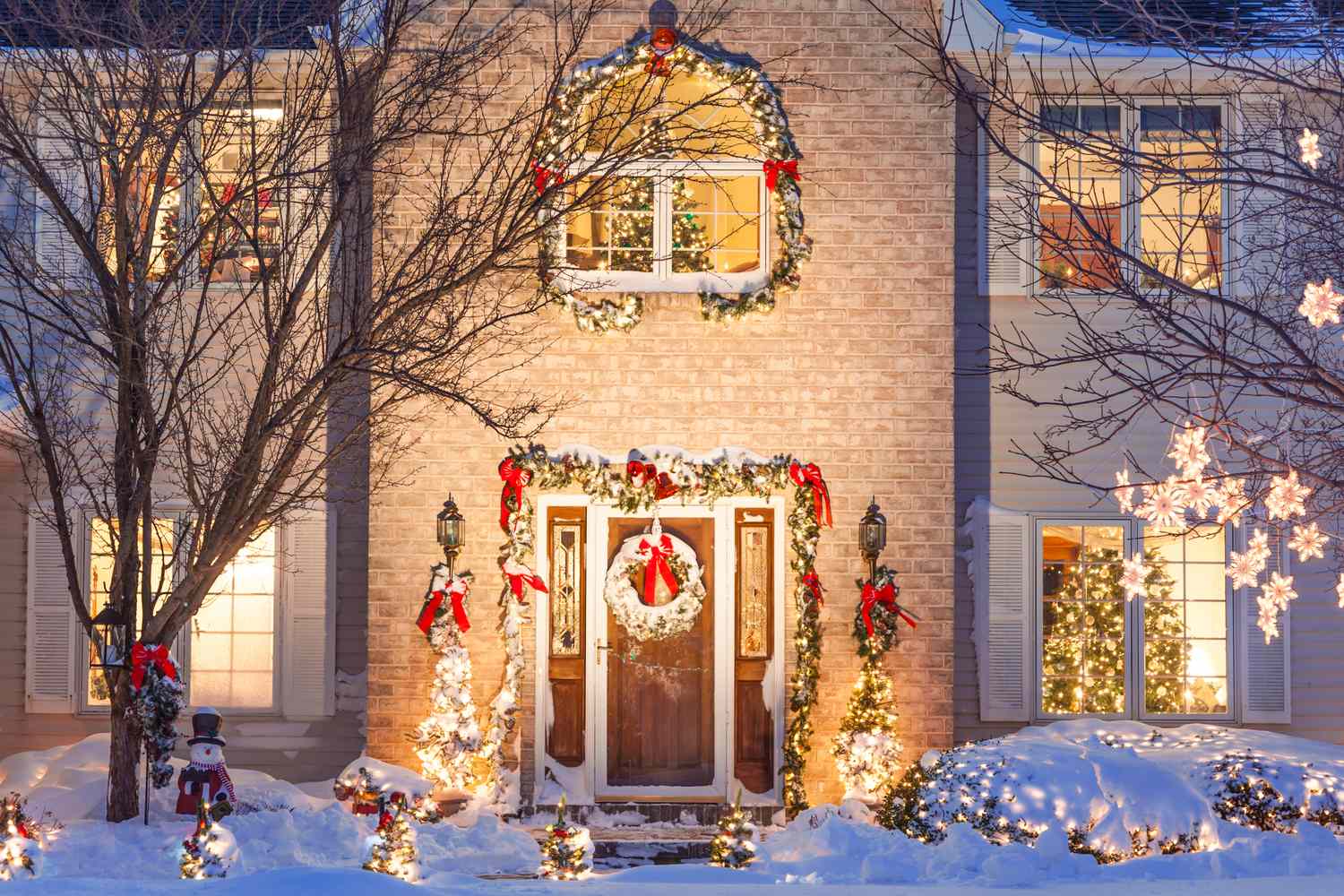 A house decorated with Christmas lights wreaths and festive ornaments with snow covering the ground and nearby trees